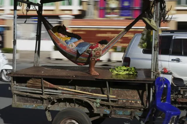 A Cambodian vendor sleeps in a hammock is carried by a motor-cart passing the Phnom Penh Municipal Court building in Phnom Penh, Cambodia, Thursday, September 15, 2022. (Photo by Heng Sinith/AP Photo)
