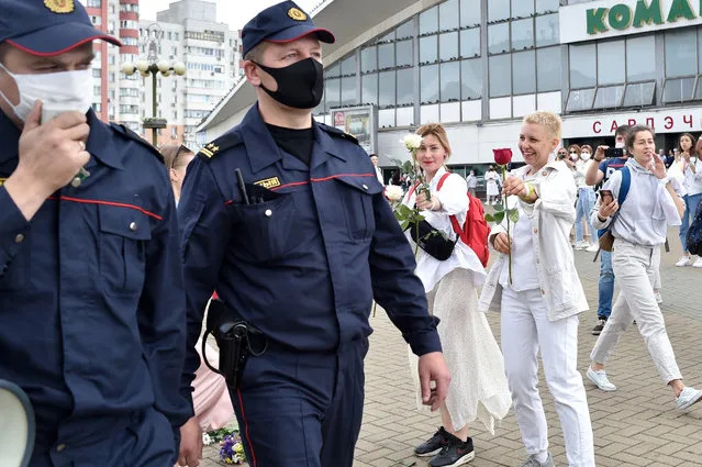 Participants of a protest against police violence during recent rallies of opposition supporters, who accuse strongman Alexander Lukashenko of falsifying the polls in the presidential election, offer flowers to two police officers passing by in Minsk on August 12, 2020. (Photo by Sergei Gapon/AFP Photo)