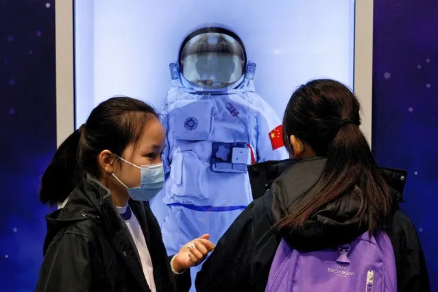 Children stand next to an image of a Chinese space suit displayed on a screen, at the InnoTech Expo in Hong Kong, China on December 13, 2022. (Photo by Tyrone Siu/Reuters)