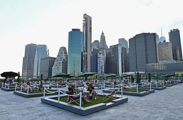 People relax on socially distant mini lawns at the rooftop of Pier 17, called “The Greens”, on August 14, 2020 in the Seaport District of New York City. The rooftop had to cancel its entire run of concerts and special events this season due to the COVID-19 pandemic. (Photo by Angela Weiss/AFP Photo)