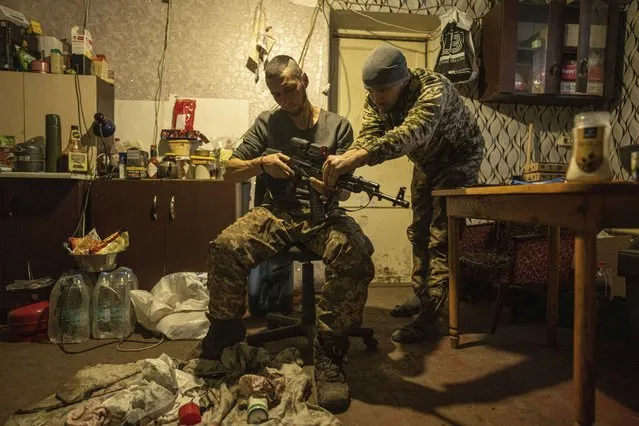 Ukrainian servicemen of Karpatska Sich battalion “Diesel”, left and “Sten”,right, install a scope on a AK-74 rifle near the recently liberated town of Lyman, Ukraine, Sunday, January 8, 2023. (Photo by Evgeniy Maloletka/AP Photo)