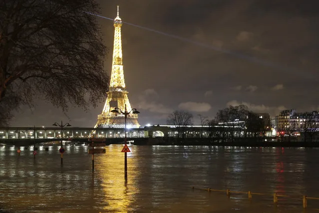 A flooded street lamp and signboards are pictured next to the river Seine in Parison the river Seine in Paris, Saturday, January 27, 2018. Floodwaters were nearing their peak in Paris on Saturday, with the rain-swollen Seine River engulfing scenic quays and threatening wine cellars and museum basements. The Eiffel tower is seen background. (Photo by Christophe Ena/AP Photo)