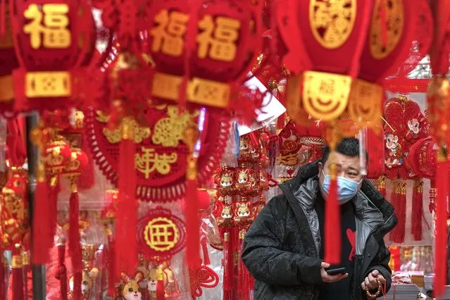 A man wearing a face mask shops for Chinese Lunar New Year decorations at a pavement store in Beijing, Saturday, January 7, 2023. (Photo by Andy Wong/AP Photo)