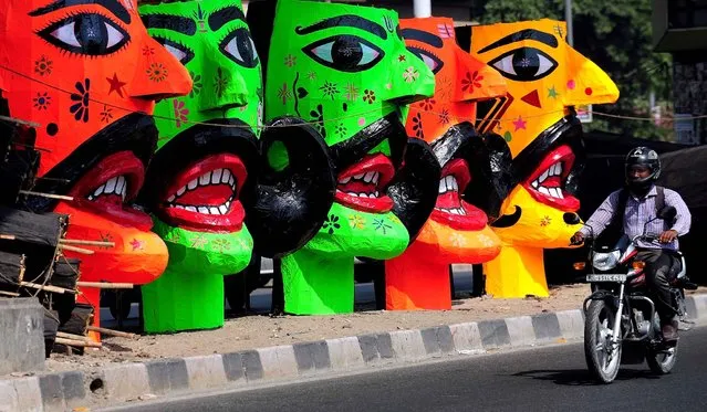 An Indian motorcyclist passes by the effigies of the demon king of Hindu Mythology, Ravana, displayed for sale at a roadside in New Delhi on October 20, 2015. Held at the end of the Navratri (nine nights) festival, Dussehra symbolises the victory of good over evil in Hindu mythology. (Photo by Prakash Singh/AFP Photo)