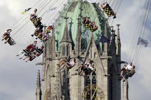 People ride a swing in front of the St. Paul's church at the 183rd Oktoberfest beer festival in Munich, Germany, Monday, September 26, 2016. The world's largest beer festival will be held from Sept. 17 to Oct. 3, 2016. (Photo by Matthias Schrader/AP Photo)