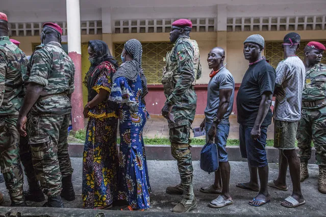 Civilians and soldiers line up to vote at the Boulbinet Deaf School in Conakry, Guinea, Sunday October 18, 2020. Guinean President Alpha Conde is seeking to extend his decade in power, facing off against his longtime rival Cellou Dalein Diallo for the third time at the polls. (Photo by Sadak Souici/AP Photo)