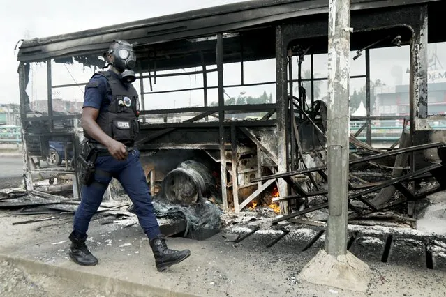 A riot police member walks next to a bus which was burned early in the morning by protesters against the Ivorian President Alassane Ouattara's decision to stand for a third term, in Abidjan, Ivory Coast on October 19, 2020. (Photo by Luc Gnago/Reuters)