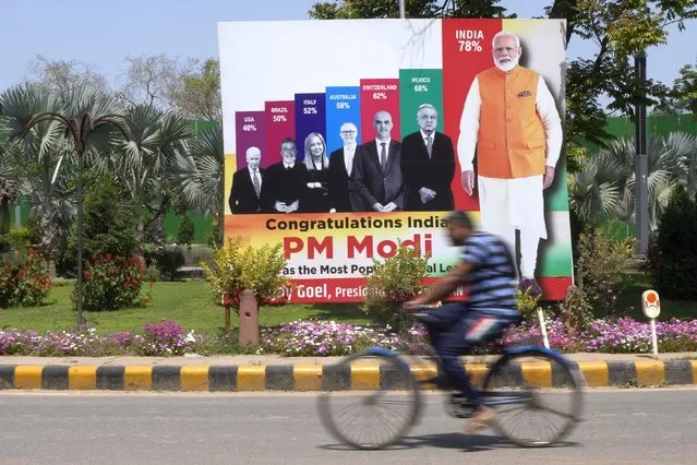 An office-goer on a bicycle rides past a huge hoarding showing Indian prime minister Narendra Modi's popularity among world leaders being the highest, in New Delhi, India, Thursday, April 6, 2023. Over 100 Congress and other opposition lawmakers hold a protest march as the Indian Parliament's budget session ends, marred by shouting and disruption of proceedings in a standoff with the Modi government. They chant slogans warning India's democracy is in danger and accuse the Modi government of “misusing” government-run investigating agencies to intimidate opposition leaders. (Photo by Manish Swarup/AP Photo)