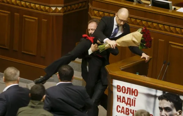 Rada deputy Oleg Barna removes Prime Minister Arseny Yatseniuk from the tribune, after presenting him a bouquet of roses, during the parliament session in Kiev, Ukraine, December 11, 2015. (Photo by Valentyn Ogirenko/Reuters)
