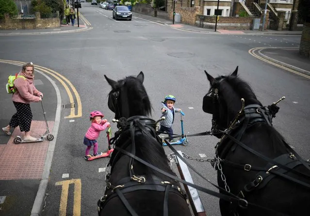 Children cross the street in front of a horse-drawn delivering different beers made by Windsor & Eton Brewery, in Windsor, England, on April 28th, 2022. Windsor & Eton brewery created the Castle Hill beer, specially to mark the Britain's Queen Elizabeth II, 70 years on the throne. “We call it Castle Hill because when the queen first came to the throne, the ascension was announced on the Castle Hill at Windsor”, explains Will Calvert, director of the Windsor & Eton brewery, which is bathed in the sweet smell of malt and hot water. (Photo by Daniel Leal/AFP Photo)