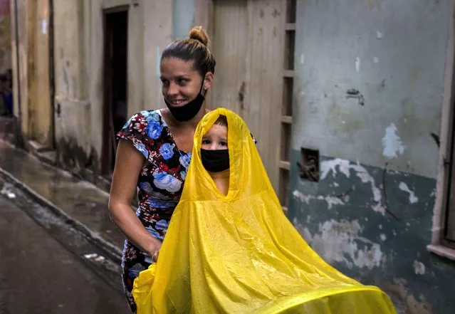 Wearing protective face masks amid the new coronavirus pandemic, a woman pushes a cart with a child wearing a raincoat during a light rain in Havana, Cuba, Friday, October 16, 2020. Cuba relaxed COVID-19 restrictions Monday in hopes of boosting its economy, allowing shops and government offices to reopen and welcoming locals and tourists at airports across the island. (Photo by Ramon Espinosa/AP Photo)