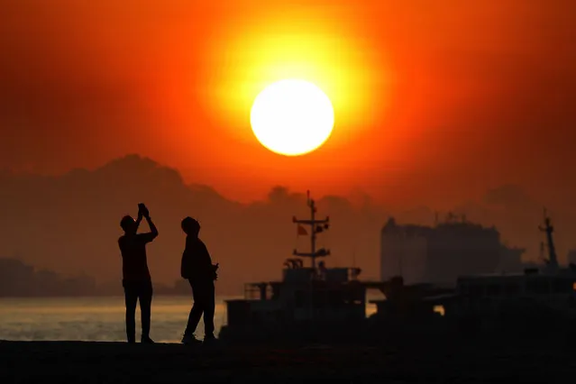 People taking photo of the sunrise are pictured with vessels anchored along the southern coast on April 2, 2021 in Singapore. (Photo by Suhaimi Abdullah/NurPhoto/Rex Features/Shutterstock)