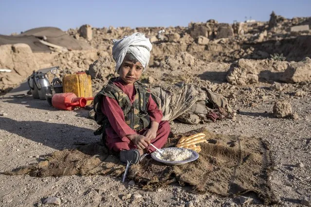 An Afghan boy eats in front of his house that was destroyed by the earthquake in Zenda Jan district in Herat province, western of Afghanistan, Wednesday, October 11, 2023. (Photo by Ebrahim Noroozi/AP Photo)