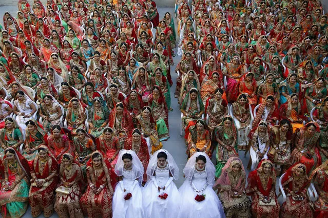 Indian brides sit together for a group photograph during a mass wedding in Surat, India, Sunday, December 23, 2018. Two hundred and sixty one young couples, including six Muslim and three Christian couples tied the knot at the mass wedding hosted by Indian businessman Mahesh Savani, who has been funding the weddings of fatherless girls in the city of Surat for several years. Weddings in India are expensive affairs with the bride's family traditionally expected to pay the groom a large dowry of cash and gifts. (Photo by Ajit Solanki/AP Photo)