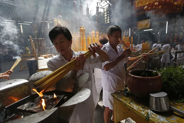 In this October 8, 2018, photo,  a woman lights long incense sticks at a Chinese temple in Bangkok, Thailand, to mark the eve of the Vegetarian Festival. During the festival that runs from Oct. 9 to 17 in 2018, worshippers refrain from eating animal products over the nine days to coincide with the celebration of the nine Chinese Emperor Gods. (Photo by Sakchai Lalit/AP Photo)