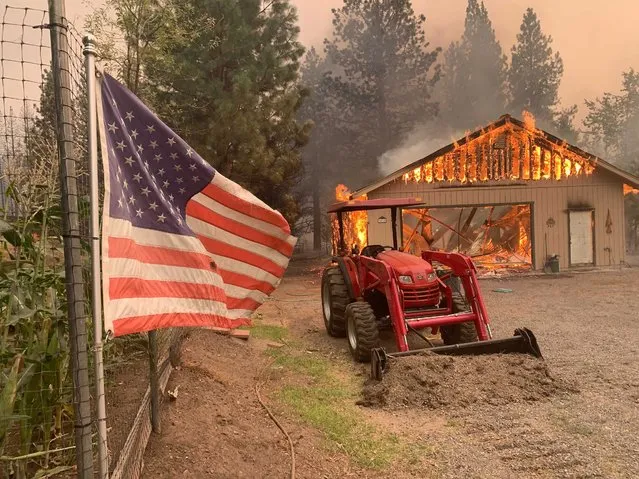 A red tractor is left behind as a home burns outside of Taylorsville in Plumas County, Calif., that was impacted by the Dixie Fire Friday, August 13, 2021. The U.S. Forest Service said Friday it's operating in crisis mode, fully deploying firefighters and maxing out its support system as wildfires continue to break out across the U.S. West. The agency says it has more than twice the number of firefighters working on the ground than at this point a year ago, and is facing "critical resources limitations." An estimated 6,170 firefighters alone are battling the Dixie Fire in Northern California, the largest of 100 large fires burning in 14 states, with dozens more burning in western Canada. It has destroyed more than 1,000 structures in the northern Sierra Nevada. (Photo by Eugene Garcia/AP Photo)