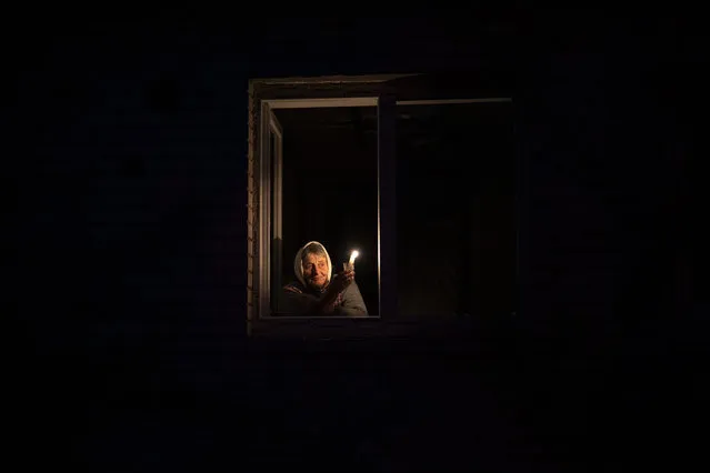 Catherine, 70, looks out the window while holding a candle for light inside her house during a power outage, in Borodyanka, Kyiv region, Ukraine, Thursday, October 20, 2022. Airstrikes cut power and water supplies to hundreds of thousands of Ukrainians on Tuesday, part of what the country's president called an expanding Russian campaign to drive the nation into the cold and dark and make peace talks impossible. (Photo by Emilio Morenatti/AP Photo)