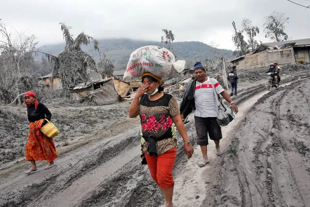 A woman weeps as she carries her belongings to a temporary shelter, following a heavy ash fall from the eruption of Mount Sinabung in Sigaranggarang, North Sumatra, Indonesia, Sunday, January 12, 2014. The volcano has sporadically erupted since September, forcing thousands of people who live around it slopes to flee their homes. (Photo by Binsar Bakkara/AP Photo)