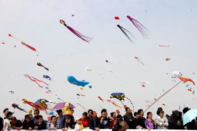 People look on as kites in various shapes fly in the sky during the International Kite Festival in Weifang, Shandong province, China April 20, 2019. (Photo by Reuters/China Stringer Network)