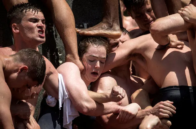 A girl supports her fellow plebes (freshmen) as they build a human pyramid to climb the 21-foot vegetable-shortening covered Herndon Monument at the U.S. Naval Academy in Annapolis, Maryland May 20, 2019. The midshipman who makes it to the top replaces the ‘dixie cup’ hat with a midshipman's hat, marking their class ascent to upperclassmen. (Photo by Kevin Lamarque/Reuters)