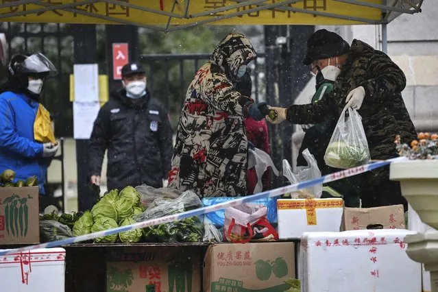 In this photo released by Xinhua News Agency, residents buy produce from a temporary market set up at the entrance of a quarantined residential area in Xi'an in northwestern China's Shaanxi Province on December 25, 2021. Xi'an, which is about 1,000 kilometers (600 miles) southwest of Beijing, reported more than 300 new cases over the weekend, a sharp rise from previous days. The city of 13 million people has been locked down, with only one person per household allowed out every two days to shop for necessities. (Photo by Tao Ming/Xinhua via AP Photo)