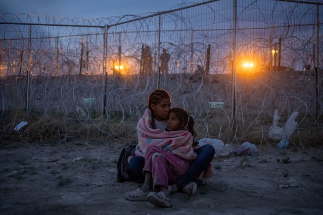 Army National Guard soldiers stand in the background as Michel, 26, of Venezuela, protects her seven-year-old daughter Aranza from Mexican immigration authorities patrolling near the dry riverbed of the Rio Grande as the migrants search for entry into the United States from the international boundary between Ciudad Juarez, Mexico and El Paso, Texas on April 24, 2024. (Photo by Adrees Latif/Reuters)