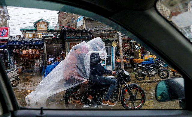 Kashmiri men take refuge under a polythene sheet to protect themselves from rainfall as they cross a bustling street on a motorcycle in Srinagar, the summer capital of Indian Kashmir, 27 April 2024. Incessant rain continues to lash over plains and higher reaches on the second consecutive day. The local meteorological department has forecast more rain during the next 48 hours in the Himalayan region. (Photo by Arooq Khan/EPA/)