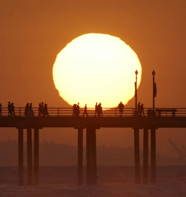 In this Saturday, May 29, 2004 file photo, people gather on a pier in Huntington Beach, Calif., as the sun sets. (Photo by Nick Ut/AP Photo)
