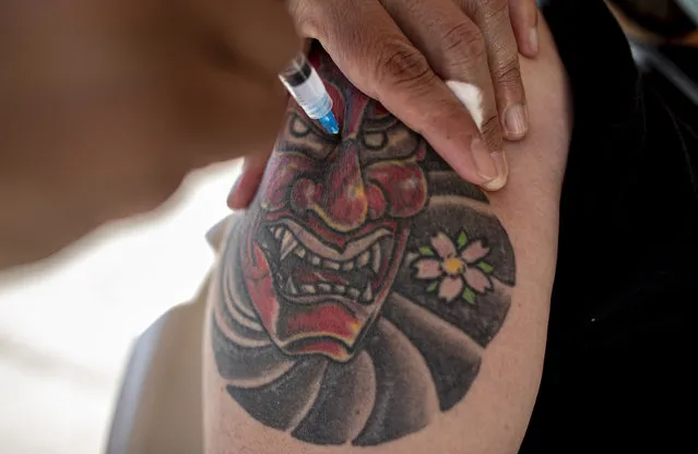 A man with a tattoo inspired on an oriental warrior mask is injected with his second dose of the Sinovac COVID-19 vaccine at a drive-thru vaccination site on the grounds of the O'Higgins Park in Santiago, Chile, Monday, April 12, 2021. (Photo by Esteban Felix/AP Photo)