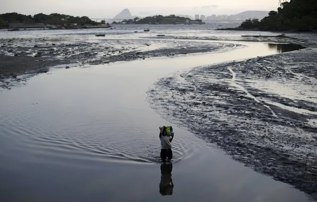 A fisherman carries a bag of fish as he walks in a channel which flows into Guanabara Bay in Rio de Janeiro Brazil, January 7, 2016. (Photo by Ricardo Moraes/Reuters)