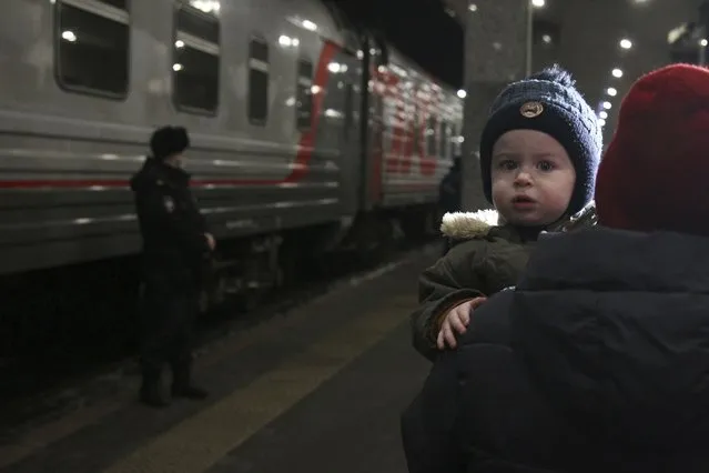A woman carries a child as they are evacuated from the Donetsk region, the territory controlled by pro-Russia separatist government in eastern Ukraine, as they leave a train to be taken to temporary accommodations, at the railway station in Nizhny Novgorod, Russia, Tuesday, February 22, 2022. A long-feared Russian invasion of Ukraine appears to be imminent, if not already underway, with Russian President Vladimir Putin ordering forces into separatist regions of eastern Ukraine. (Photo by Roman Yarovitcyn/AP Photo)