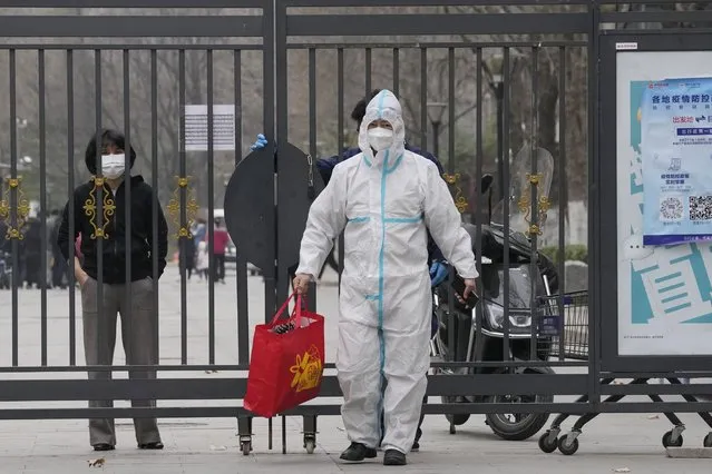 A worker in protective gear helps pass on a bag from a resident inside a locked down community on Sunday, March 13, 2022, in Beijing. The number of new coronavirus cases in an outbreak in China's northeast tripled Sunday and authorities tightened control on access to Shanghai in the east, suspending bus service to the city of 24 million and requiring a virus test for anyone who wants to enter. (Photo by Ng Han Guan/AP Photo)