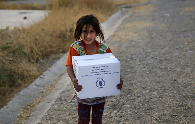 A Syrian girl who was displaced by the Turkish military operation in northeastern Syria, carries a box of food supplies at the Bardarash refugee camp, north of Mosul, Iraq, Thursday, October 17, 2019. Hundreds of refugees have crossed into Iraq in the past week, mostly through unofficial border points. On Wednesday, a first group of 890 people were bused to the Bardarash camp, in northern Iraq's semi-autonomous Kurdish region, which up until two years ago housed displaced people from the Iraqi city of Mosul. (Photo by Hussein Malla/AP Photo)
