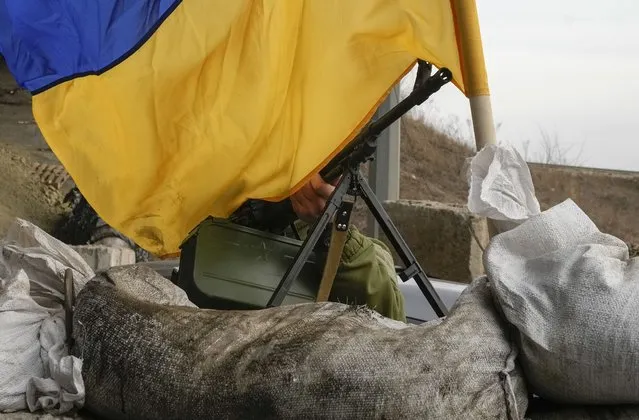 A machine gun emerges from under a Ukrainian national flag on a front line position near Kharkiv, Ukraine, Saturday, March 26, 2022. (Photo by Efrem Lukatsky/AP Photo)