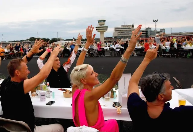 Guests wave for a helicopter as they attend an open-air event called “Freedom Dinner” on the grounds of the former Tegel Airport in Berlin, Germany, 07 August 2021. Around 3,000 guests are attending the evening event, celebrating freedom and diversity in the city of Berlin. (Photo by Filip Singer/EPA/EFE)
