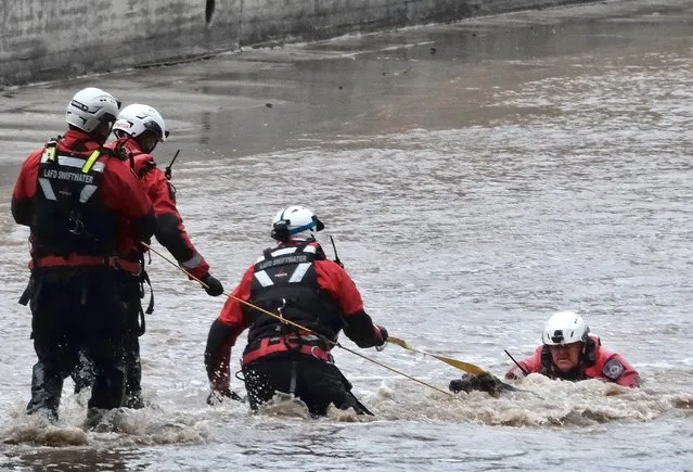 A Los Angeles Fire Department rescue crew pull a dog from the LA river in the Studio City section of Los Angeles on Monday, March 28, 2022. Two people and a dog were rescued from a rain-swollen Southern California river Monday as a vigorous late-season storm moved slowly through the state, bringing heavy showers and snow. A helicopter rescue crew pulled the dog's owner, a woman, from the rushing Los Angeles River, in the San Fernando Valley, around 2:40 p.m. But the dog slipped away and continued for more than an hour down the river, which runs through an inaccessible channel with high concrete walls for several miles. (Photo by Richard Vogel/AP Photo)
