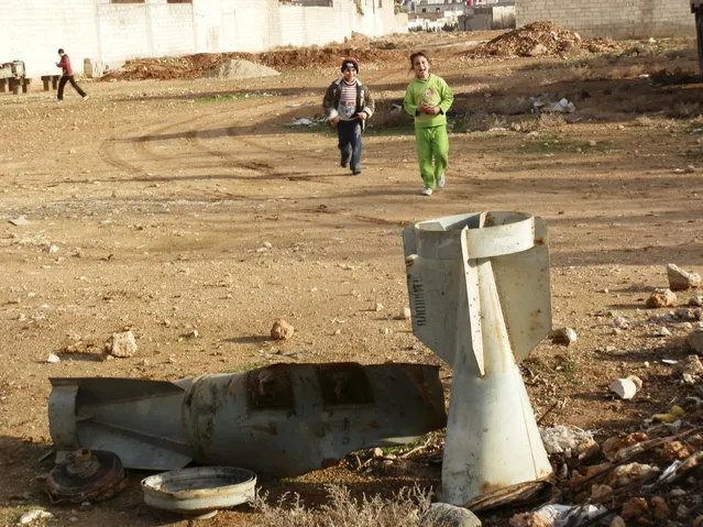 Children play near the remnants of a bomb shell in the ground, which activists said were fired by a Syrian Air Force fighter jet loyal to Syria's President Bashar al-Assad, in Daraya near Damascus December 23, 2012. (Photo by Fadi Al-Derani/Reuters/Shaam News Network)