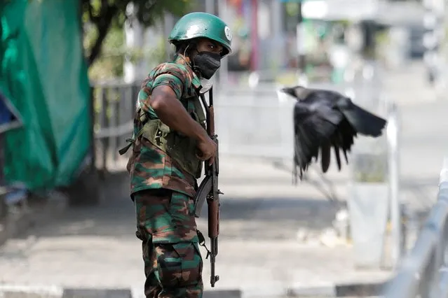 A crow flies by as a Sri Lankan army soldier stands guard on a main road after the government imposed a curfew following a clash between police and protestors near Sri Lankan President Gotabaya Rajapaksa's residence during a protest last Thursday, amid the country's economic crisis, in Colombo, Sri Lanka on April 3, 2022. (Photo by Dinuka Liyanawatte/Reuters)