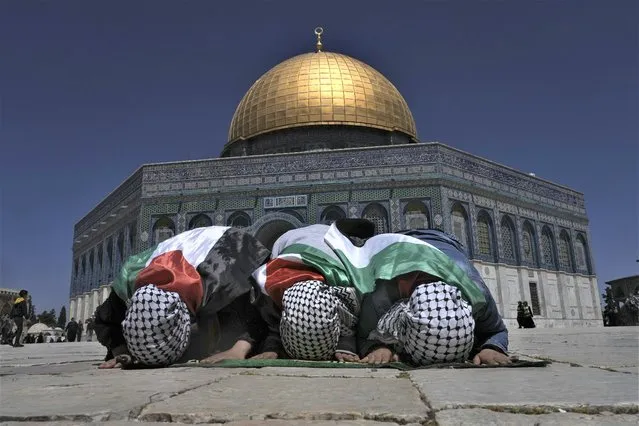 Muslim worshippers wrapped in Palestinian flags pray during holy Islamic month of Ramadan in front of the Dome of the Rock shrine at the Al Aqsa Mosque compound in Jerusalem's Old City, Friday, April 15, 2022. Palestinians clashed with Israeli police at the Al-Aqsa mosque compound in Jerusalem before dawn on Friday as thousands gathered for prayers during the holy month of Ramadan. Medics said that more than 150 Palestinians were wounded. (Photo by Mahmoud Illean/AP Photo)