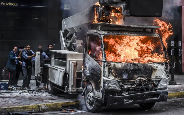 Supreme Justice Court (TSJ) workers push a truck set ablaze by opposition demostrators away from the TSJ premises during clashes of opposition activists and riot police ensueing a protest against the government of President Nicolas Maduro in Caracas on June 7, 2017. The head of the Venezuelan military, General Vladimir Padrino Lopez, who is also President Nicolas Maduro's defence minister, is warning his troops not to commit “atrocities” against protesters demonstrating in the country's deadly political crisis. Tuesday's warning came after more than two months of violent clashes between protesters and security forces. (Photo by Juan Barreto/AFP Photo)