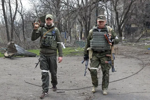 Armed servicemen of Donetsk People's Republic militia look at a photographer as they carry captured weapons in an area controlled by Russian-backed separatist forces in Mariupol, Ukraine, Friday, April 15, 2022. Mariupol, a strategic port on the Sea of Azov, has been besieged by Russian troops and forces from self-proclaimed separatist areas in eastern Ukraine for more than six weeks. (Photo by Alexei Alexandrov/AP Photo)