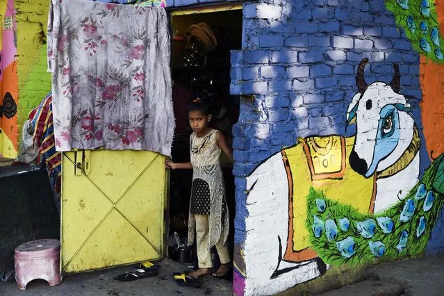 A child peers out of her home adorned with a mural painted by artists from “Delhi Street Art” group at the Raghubir Nagar slum in New Delhi on December 2, 2019. (Photo by Sajjad Hussain/AFP Photo)