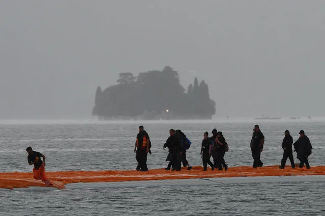 People work under heavy rain on the monumental installation “The Floating Piers” created by artists Christo and Jeanne-Claude on June 15, 2016 on the lake Iseo, northern Italy. Some 200,000 floating cubes create a 3-kilometers runway connecting the village of Sulzano to the small island of Monte Isola on the Iseo Lake for a 16-day outdoor installation opening on June 18. (Photo by Filippo Monteforte/AFP Photo)