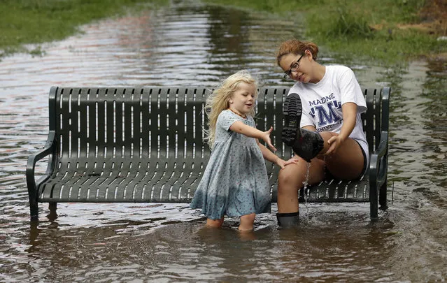 Katie Bender gets some assistance from Johanna Bender, left, as they dump water from a boot while sitting on a flooded street after Hurricane Arthur passed through in Manteo, N.C., Friday, July 4, 2014. Arthur began moving offshore and away from North Carolina's Outer Banks early Friday after hitting the state's barrier islands overnight, creating a Fourth of July holiday that saw flooding and tens of thousands of power outages. (Photo by Gerry Broome/AP Photo)