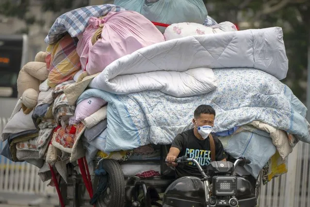 A man wearing a face mask drives a cart loaded with bedding and fabric along a street in Beijing, Thursday, June 16, 2022. (Photo by Mark Schiefelbein/AP Photo)