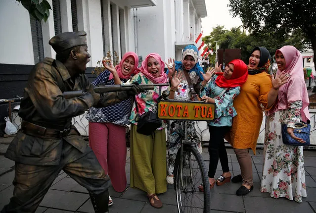 Tourists pose for a  picture with a street performer dressed as an Indonesian soldier in Jakarta's Old Town, Indonesia August 2, 2017. (Photo by Reuters/Beawiharta)