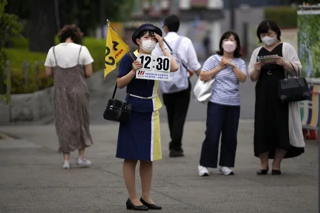 A tour guide wearing a protective mask to help curb the spread of the coronavirus holds a banner showing an assembly time for her tour group near a shopping street at the Asakusa district, Friday, June 10, 2022, in Tokyo. (Photo by Eugene Hoshiko/AP Photo)
