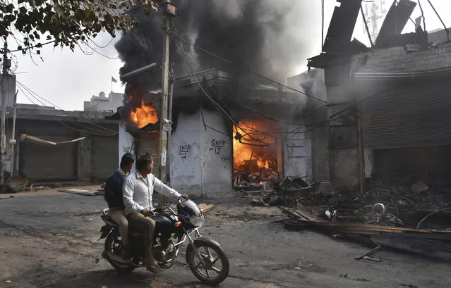 A motorcyclist drives past shops that were set on fire by mobs in New Delhi, India, Wednesday, February 26, 2020. At least 20 people were killed in three days of clashes in New Delhi, with the death toll expected to rise as hospitals were overflowed with dozens of injured people, authorities said Wednesday. The clashes between Hindu mobs and Muslims protesting a contentious new citizenship law that fast-tracks naturalization for foreign-born religious minorities of all major faiths in South Asia except Islam escalated Tuesday. (Photo by Dinesh Joshi/AP Photo)