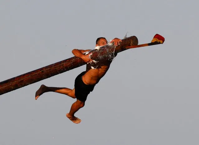 A competitor tries to grab a flag as he falls off the "gostra", a pole covered in lard, during the week-long celebrations of the religious feast of St. Julian, patron of the town of St. Julian's, Malta on August 20, 2022. (Photo by Darrin Zammit Lupi/Reuters)