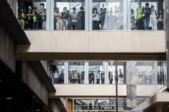 Bystanders watch from footbridges as riot police (not seen) stand guard outside a building below in Hong Kong on May 27, 2020, as the city's legislature debates over a law that bans insulting China's national anthem. Hong Kong police cast a dragnet around the financial hub's legislature on Wednesday, firing pepper-ball rounds and arresting hundreds as they stamped down on protests against a bill banning insults to China's national anthem. (Photo by Anthony Wallace/AFP Photo)